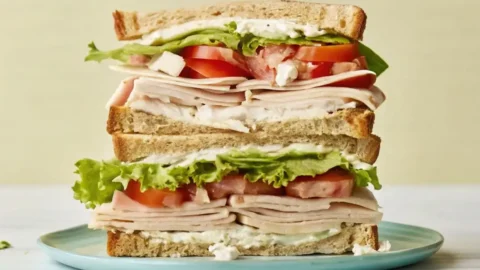 Layered turkey cheese sandwich with sliced turkey, cheese spread, lettuce, and tomato stacked between toasted bread.