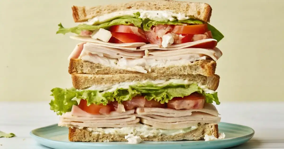Layered turkey cheese sandwich with sliced turkey, cheese spread, lettuce, and tomato stacked between toasted bread.